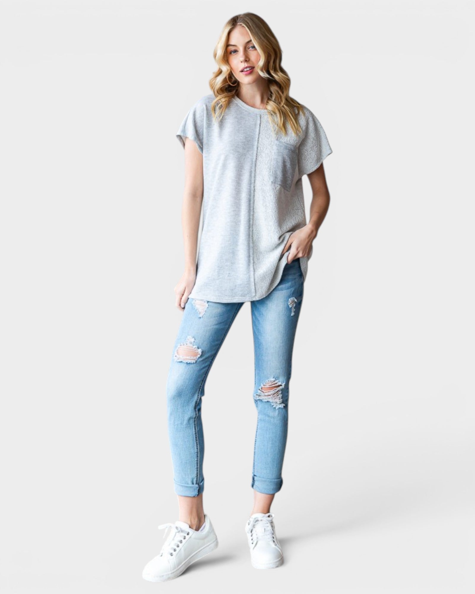 Woman wearing a gray t-shirt and light blue ripped jeans on a white background