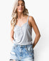 A woman wearing a light gray ribbed camisole top with a button henley detail and distressed blue denim jeans, photographed against a clean white studio background.