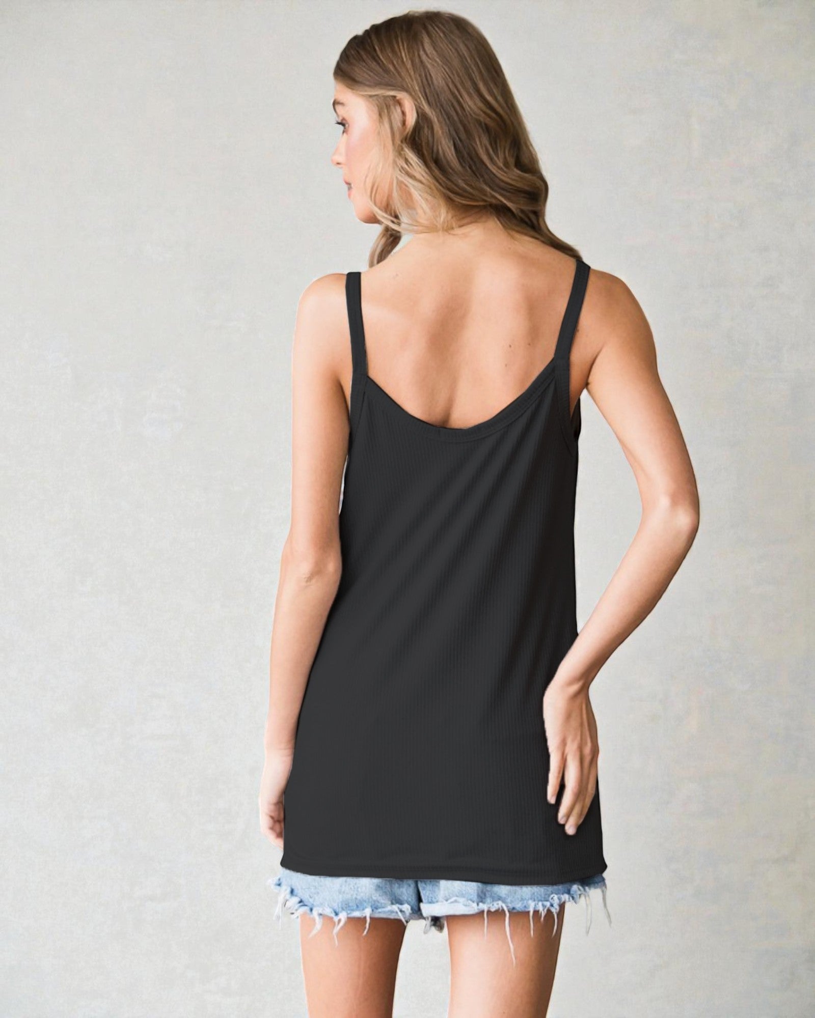 Woman wearing a black tank top and denim shorts on a plain background