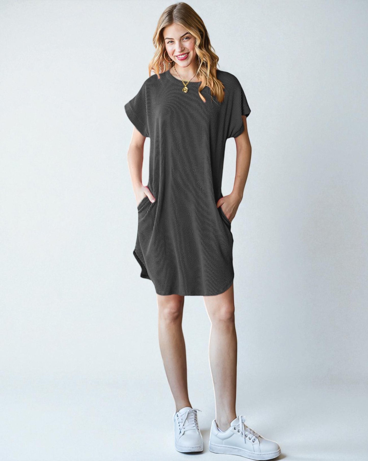 Woman wearing a dark gray t-shirt dress with white sneakers on a light background