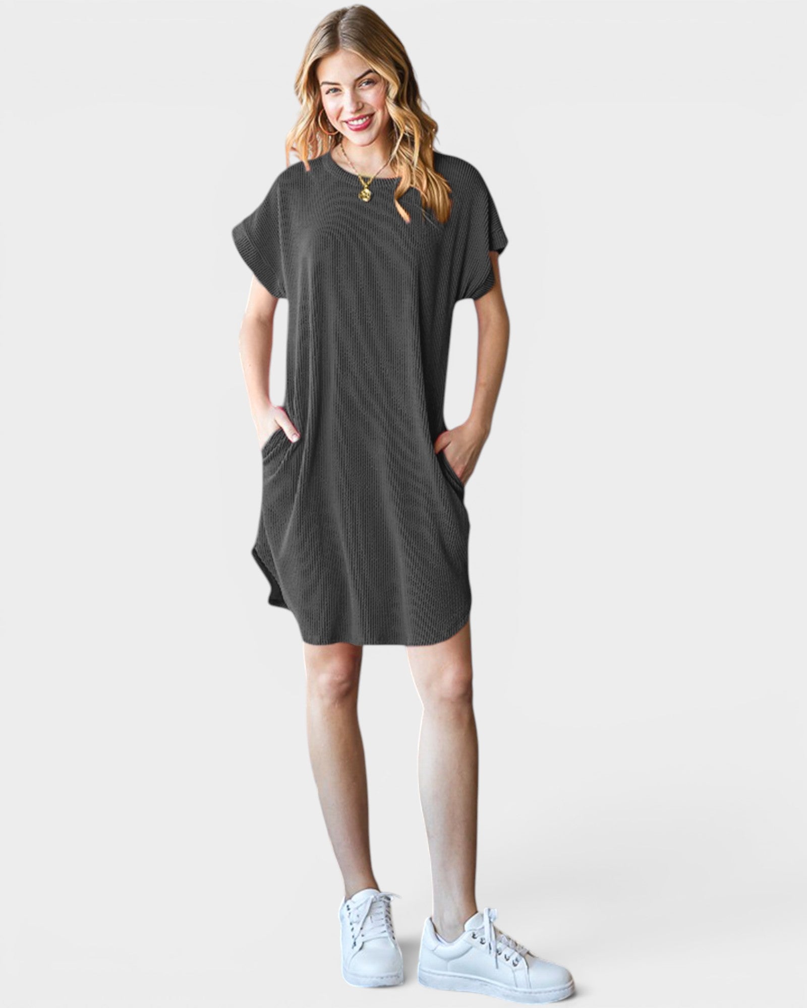 Woman wearing a dark gray t-shirt dress with white sneakers on a light gray background
