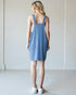 Woman wearing a blue dress standing against a plain white wall.