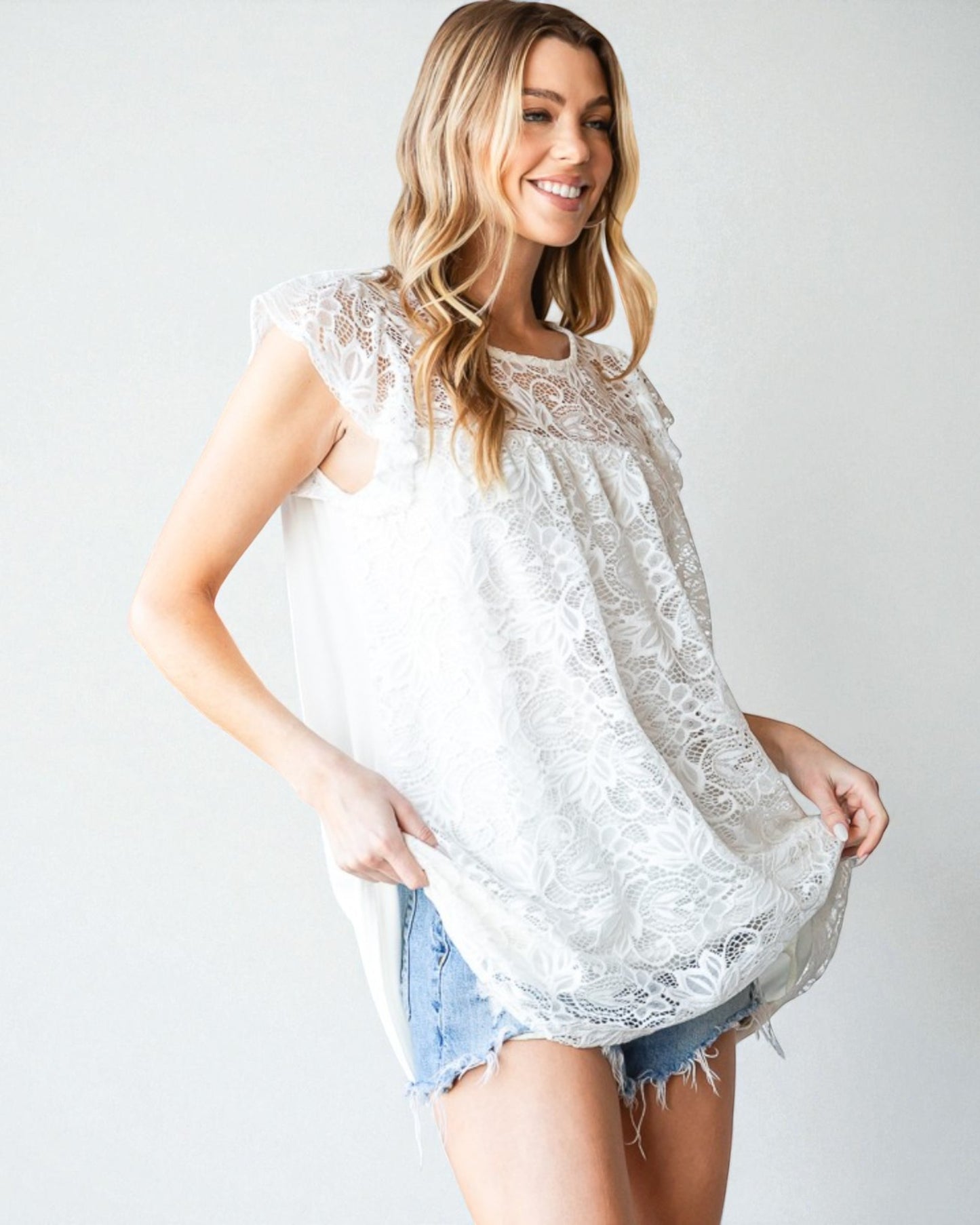 Woman wearing a white lace top and denim shorts on a plain background