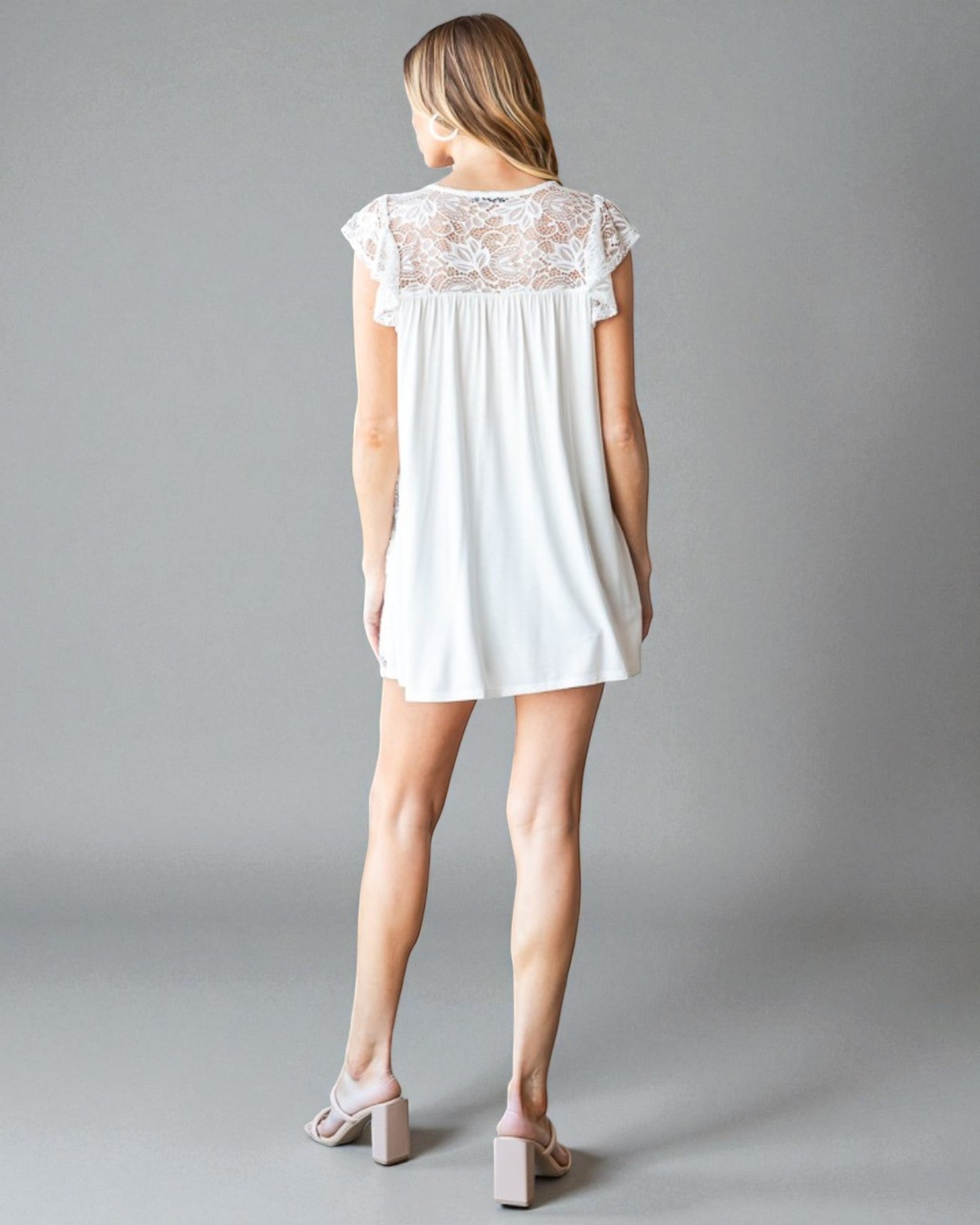 Woman wearing a white lace-trimmed dress on a gray background