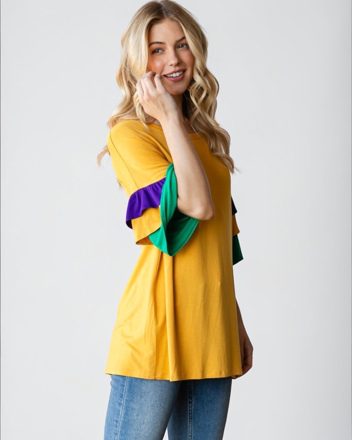 Woman wearing a mustard yellow top with colorful sleeves on a white background