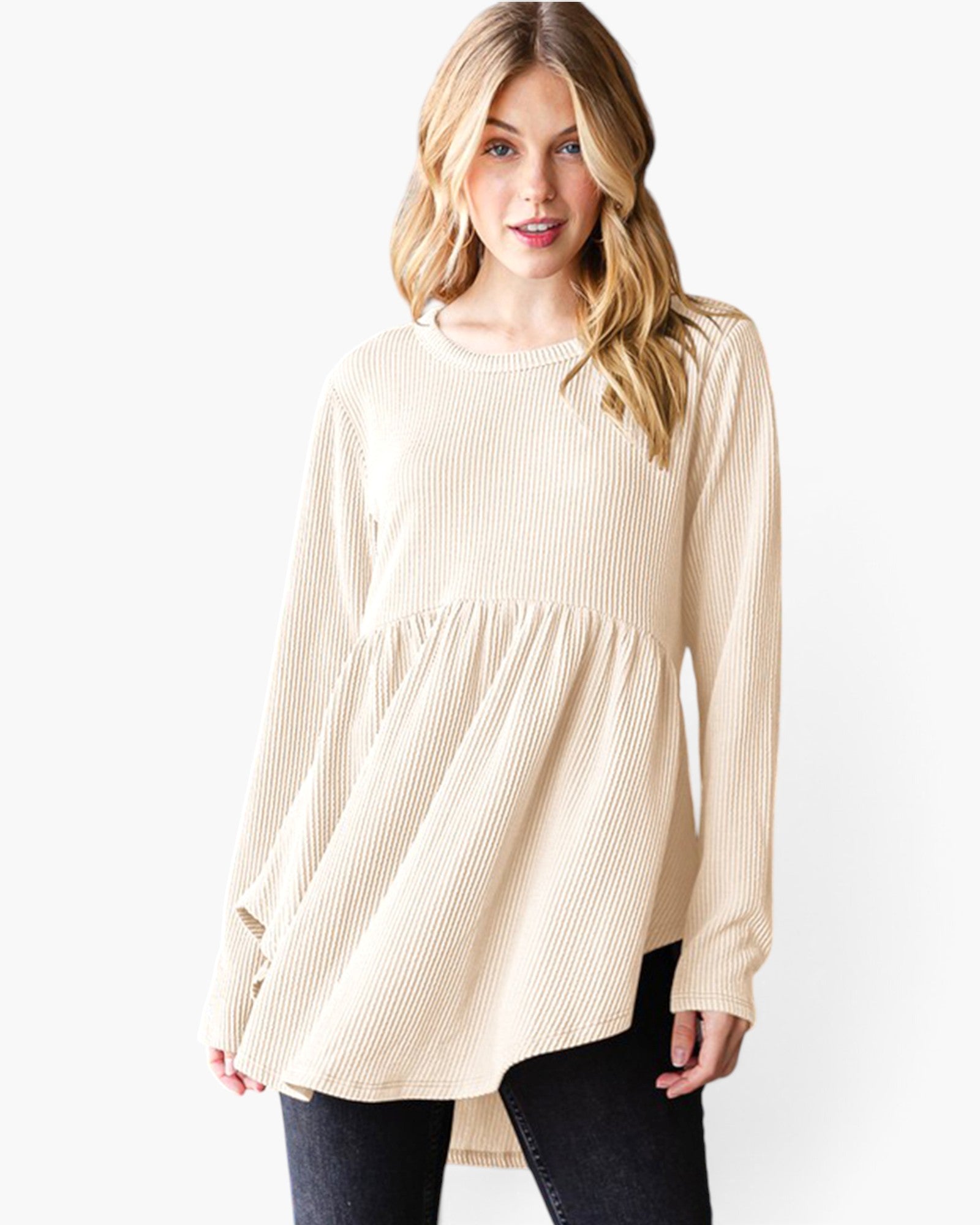 A woman modeling a cream-colored, long-sleeve ribbed knit top with a gathered peplum waist, paired with dark jeans, against a plain white background.