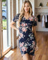 Woman wearing a navy floral dress in a room with wooden flooring and a clothing rack.