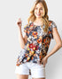 Woman wearing a colorful floral top and white shorts against a plain background