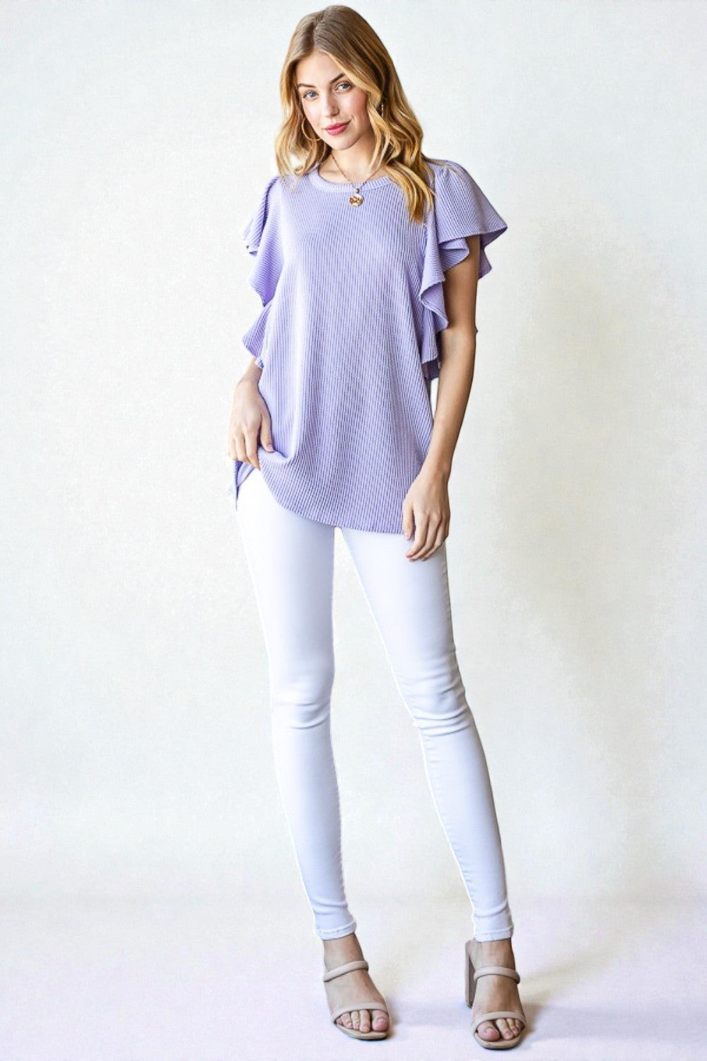 Woman wearing a light purple top and white pants against a white background