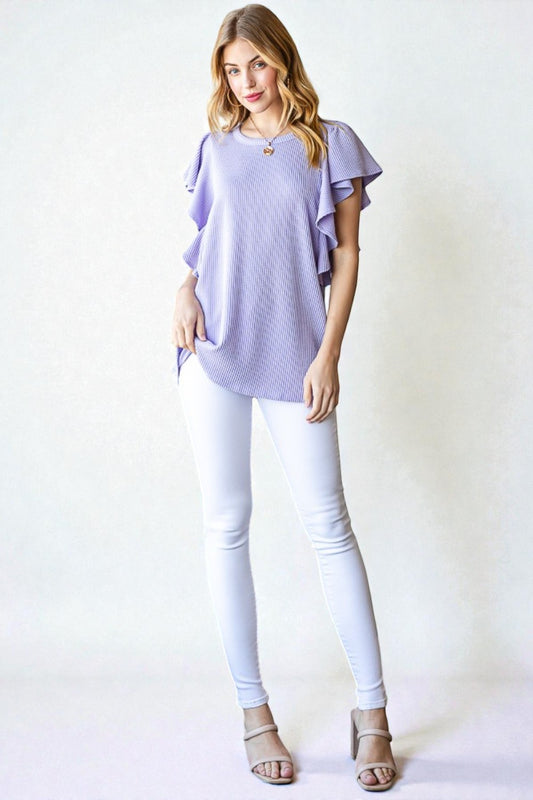 Woman wearing a light purple top and white pants against a white background