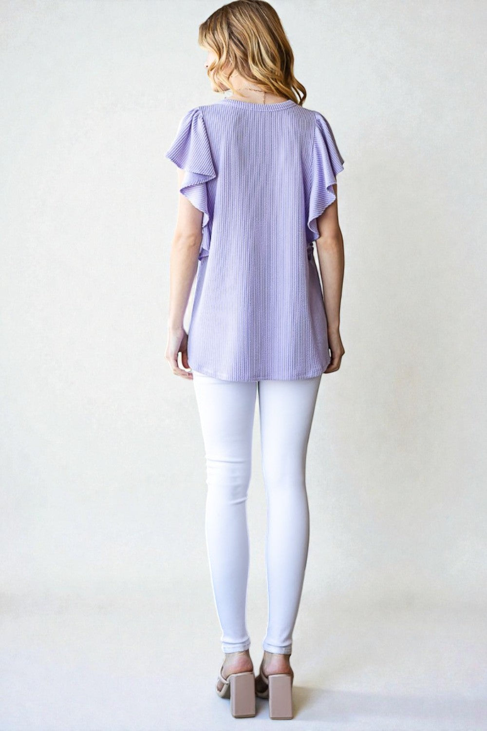 Woman wearing a light purple top and white pants on a plain background