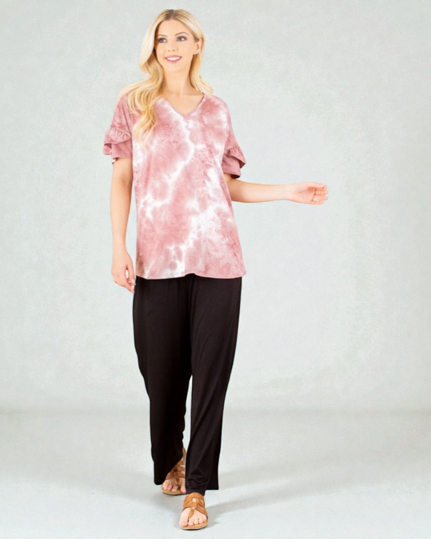 Woman wearing a pink tie-dye top and black pants on a white background