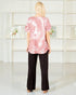 Woman wearing a pink tie-dye top and black pants standing in front of a white shelving unit.