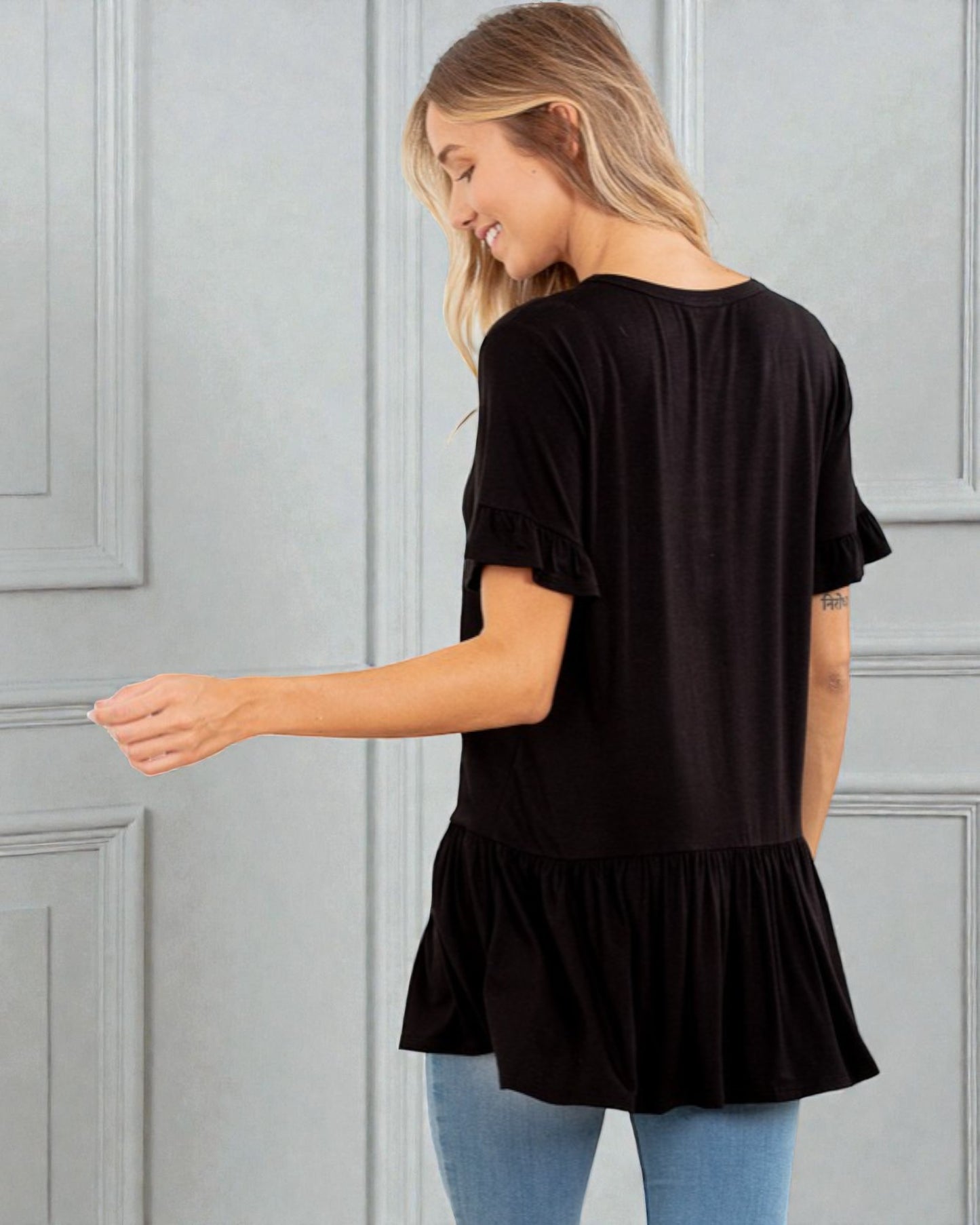 Woman wearing a black ruffled blouse against a gray paneled wall