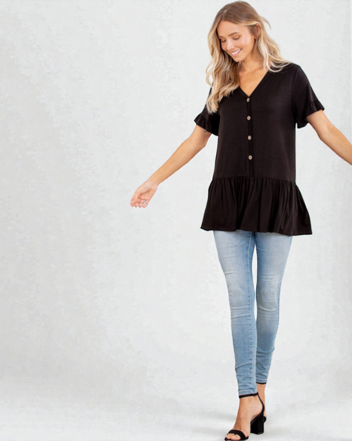 Woman wearing a black ruffled blouse and light blue jeans on a white background