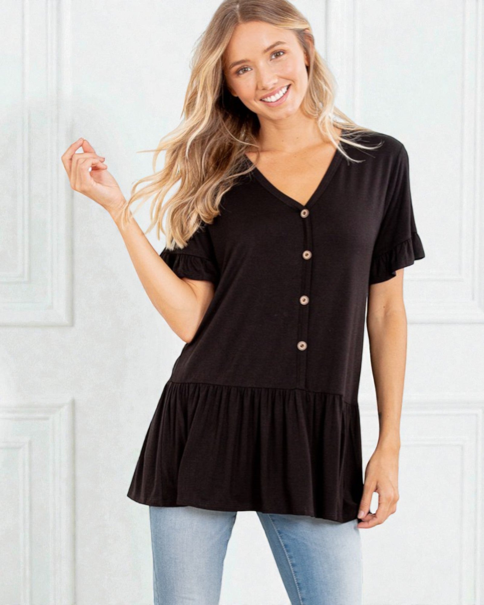 Woman wearing a black short-sleeve top with buttons and a layered skirt against a white background