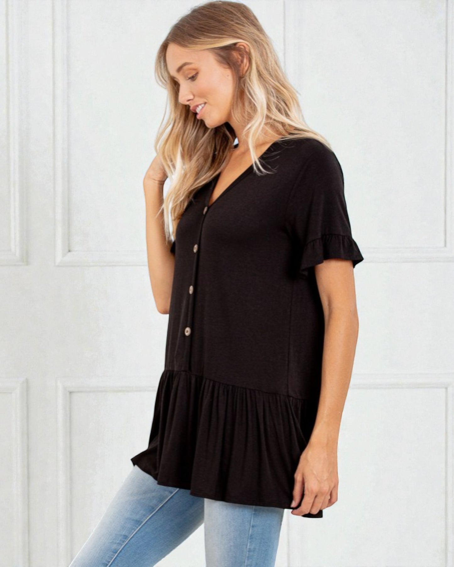 Woman wearing a black tiered blouse with blue jeans against a white background