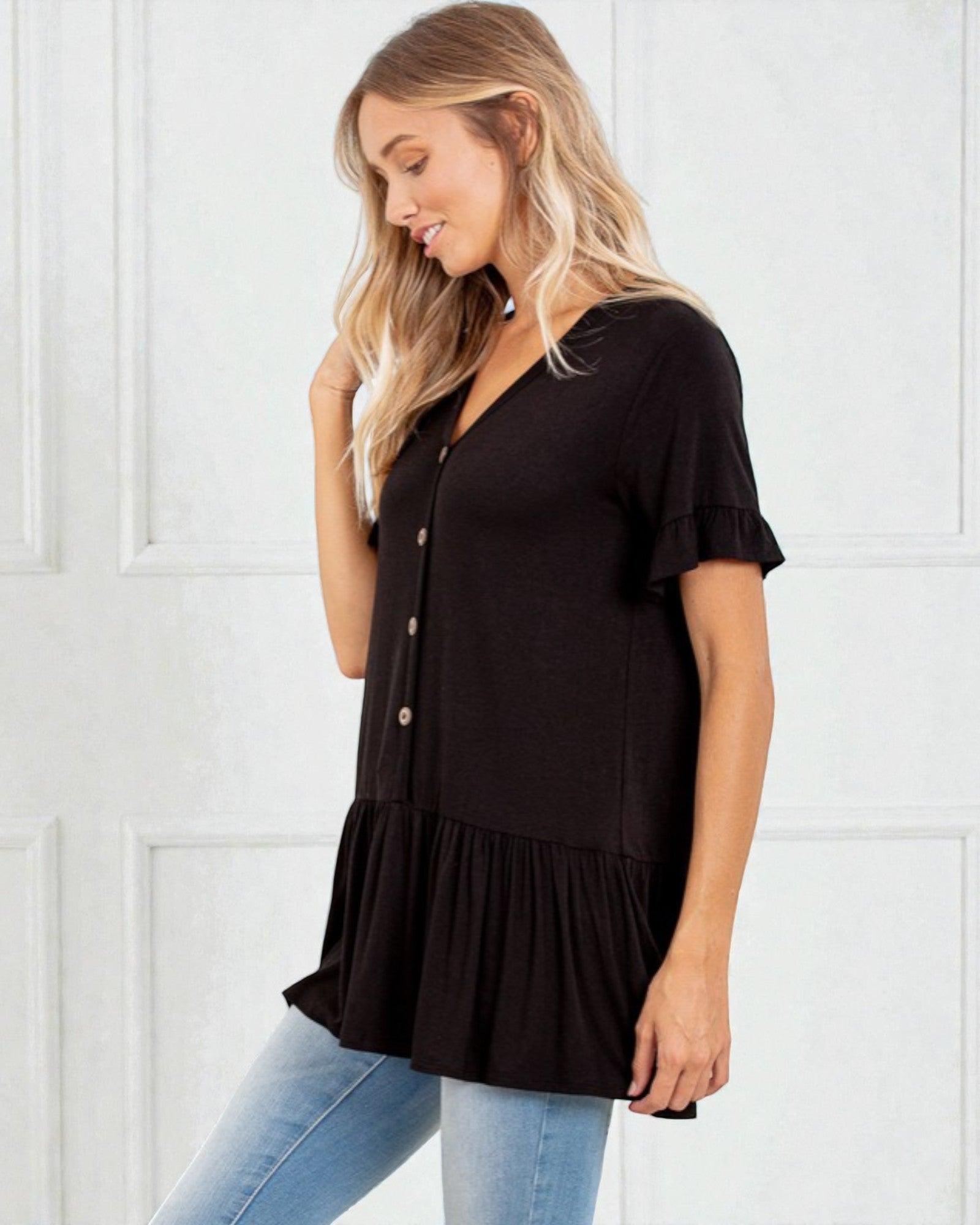 Woman wearing a black tiered blouse with blue jeans against a white background