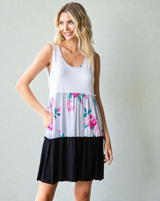 Woman wearing a white tank top with floral skirt and black bottom on a plain background