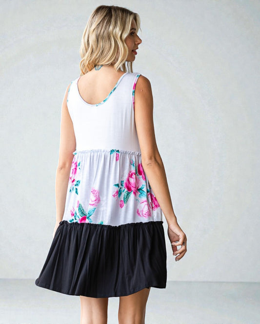 Woman wearing a dress with floral top and black bottom on a plain background