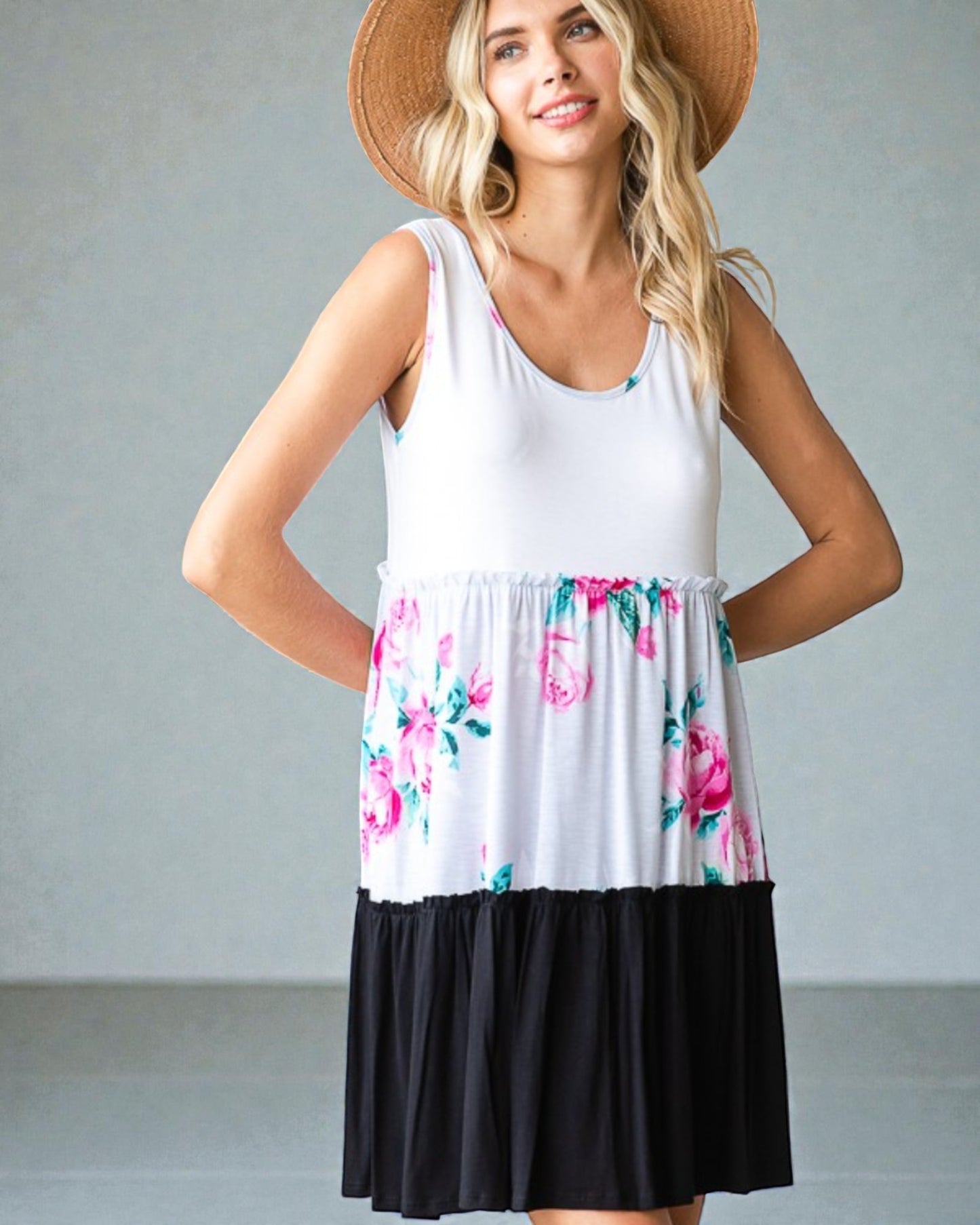 Woman wearing a white sleeveless dress with floral pattern and black bottom half, standing against a plain background.