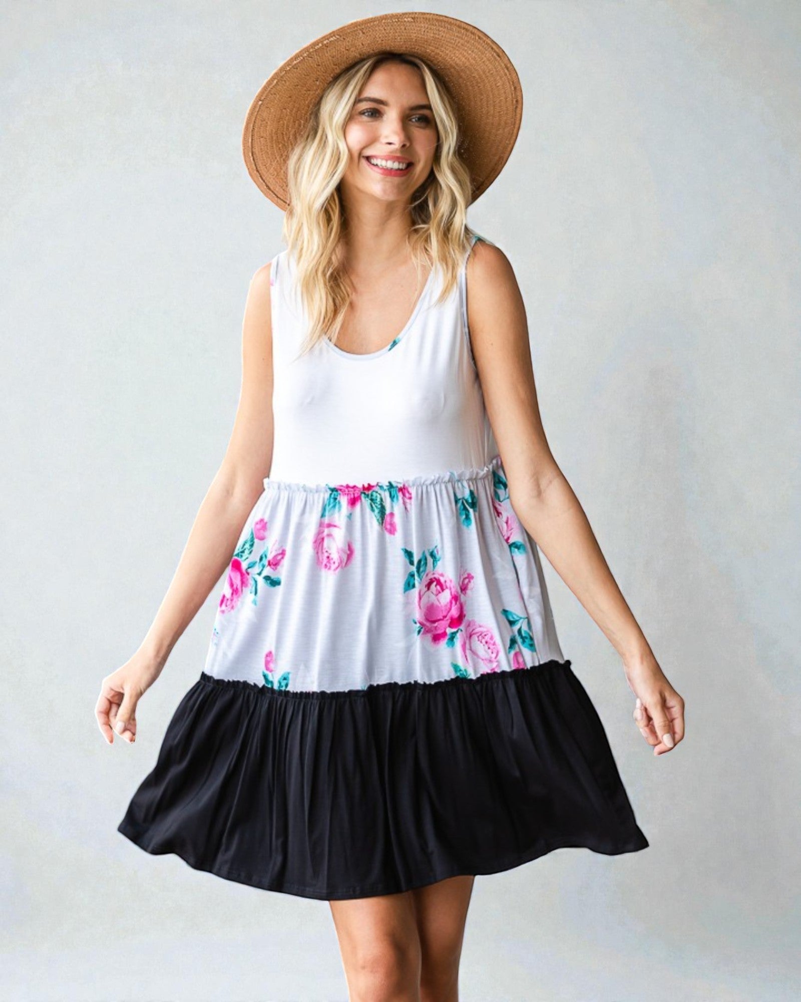 Woman wearing a white sleeveless top with floral skirt and black bottom, standing against a plain background.