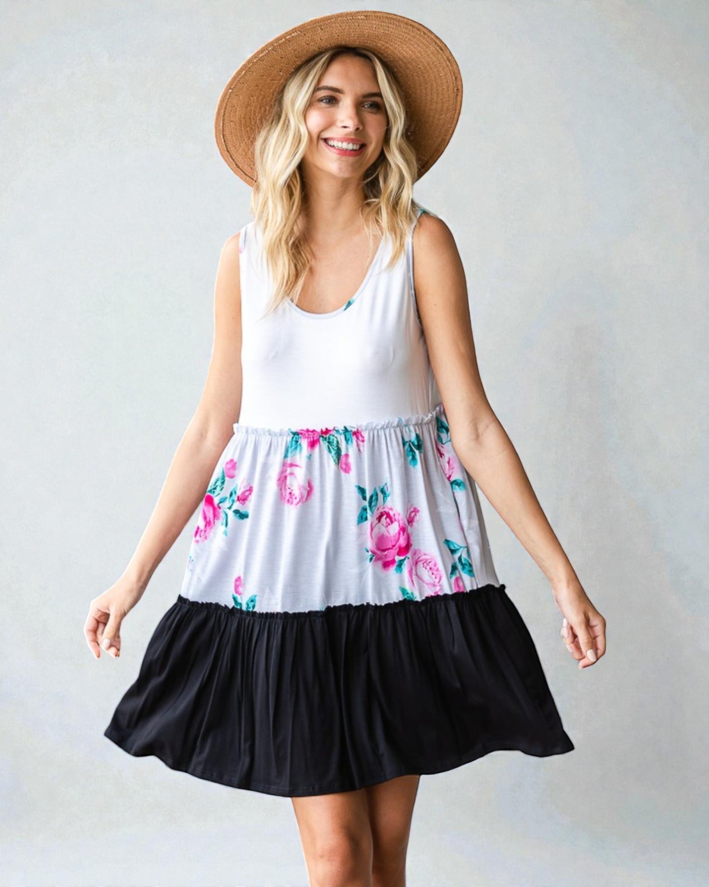 Woman wearing a white sleeveless top with floral skirt and black bottom, standing against a plain background.
