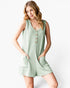 A woman modeling a sleeveless, light sage green romper with vertical pinstripes, a button-down front, and side pockets, set against a plain white studio background.