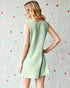 Woman wearing a green sleeveless dress against a patterned wall.