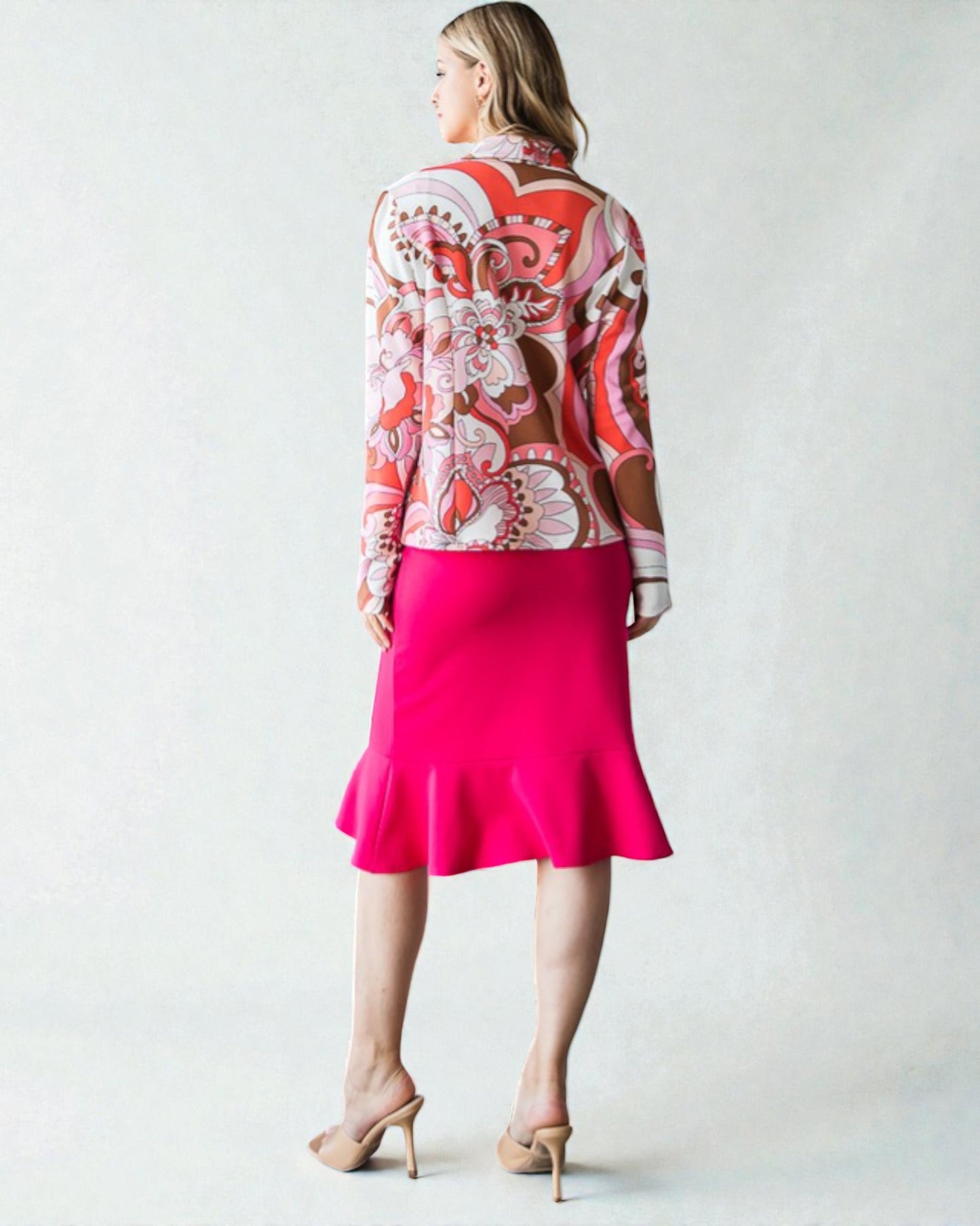 Woman wearing a patterned jacket and bright pink skirt on a white background