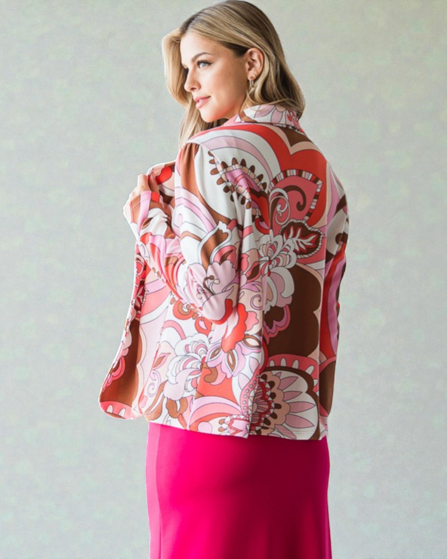 Woman wearing a colorful patterned jacket and pink skirt against a plain background