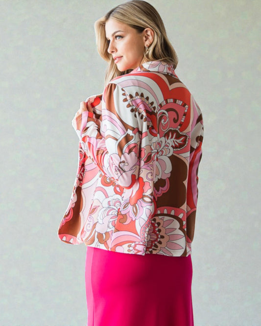 Woman wearing a colorful patterned jacket and pink skirt against a plain background