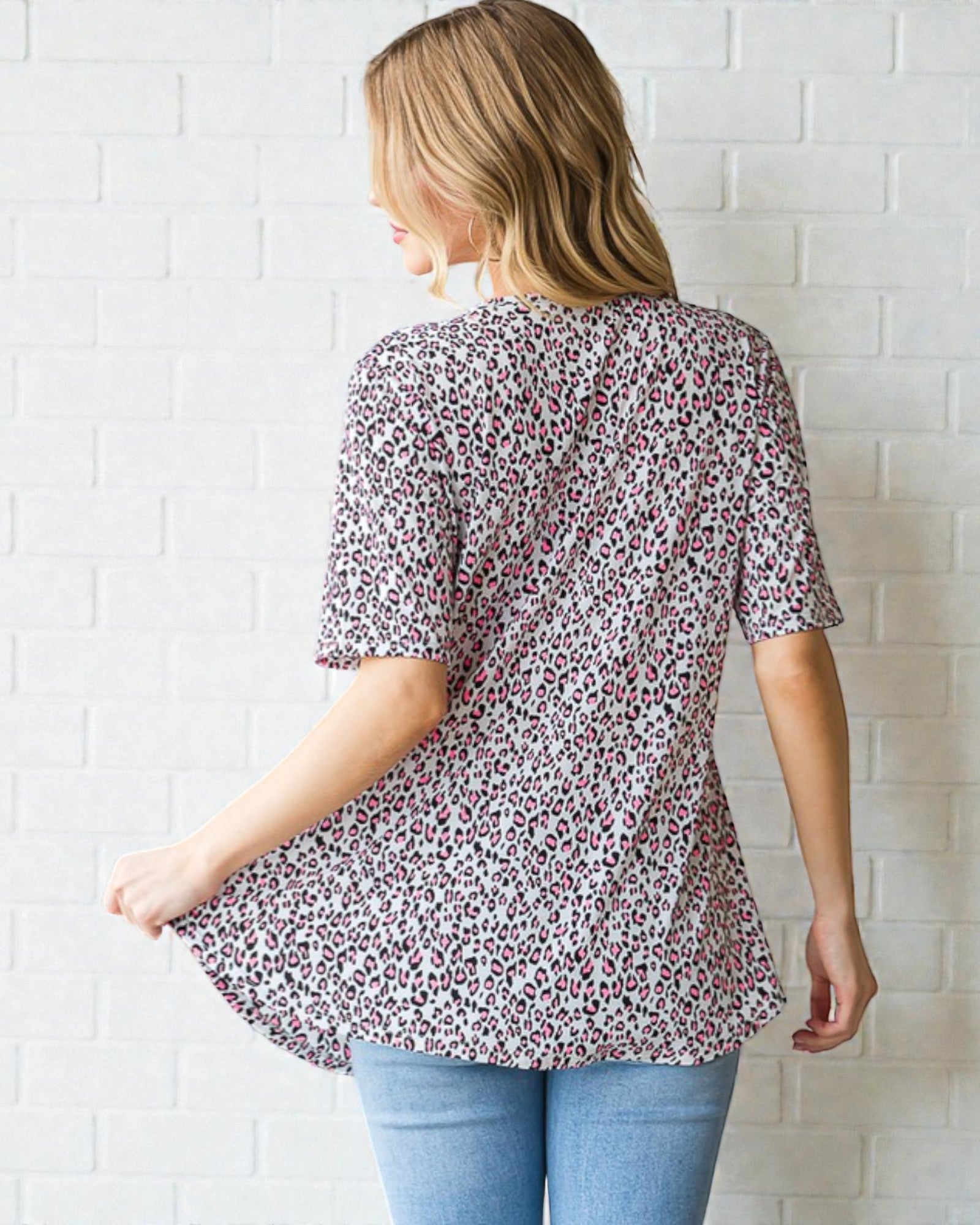 Woman wearing a floral blouse and blue jeans against a white brick wall.