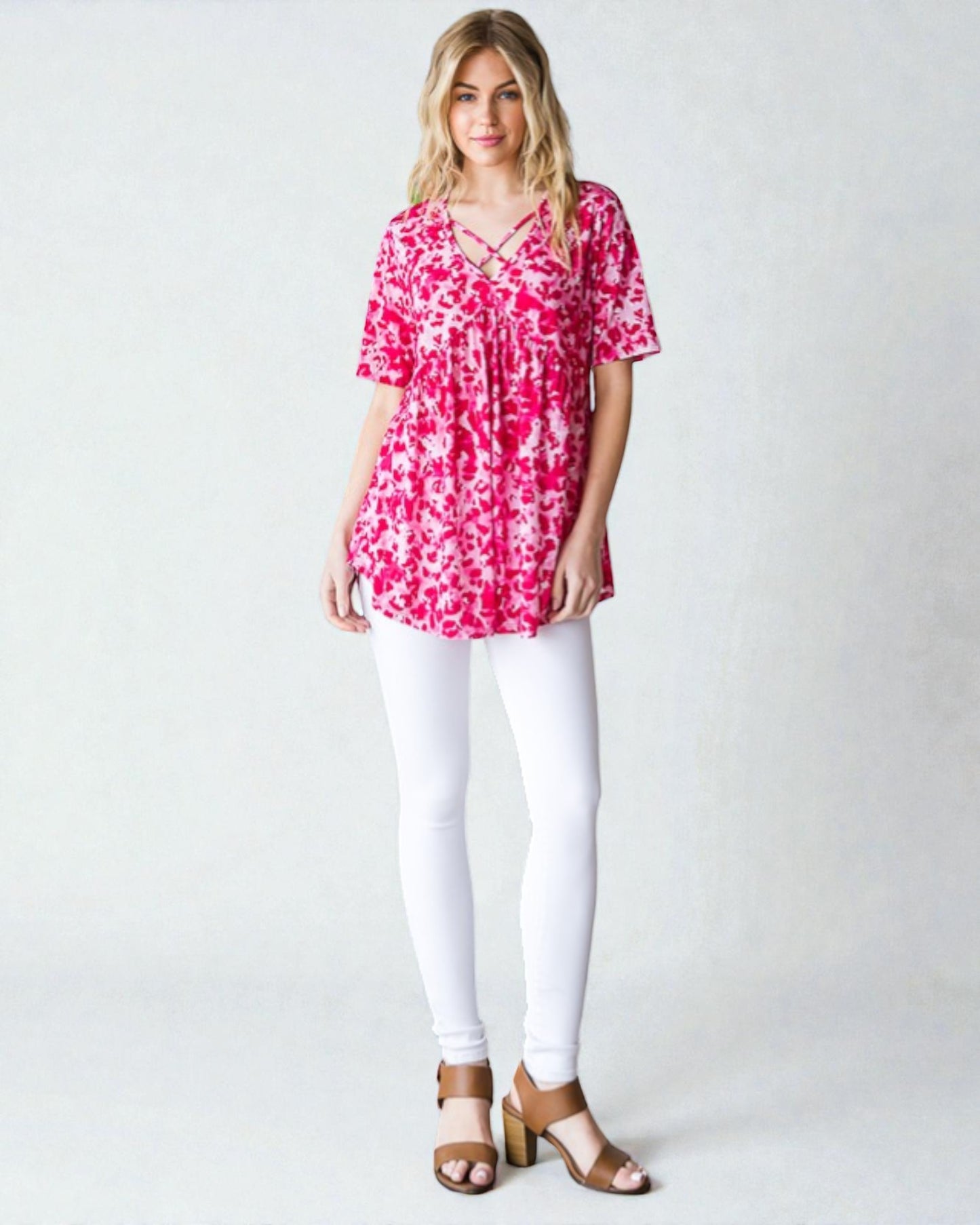 Woman wearing a pink floral top and white pants on a plain background