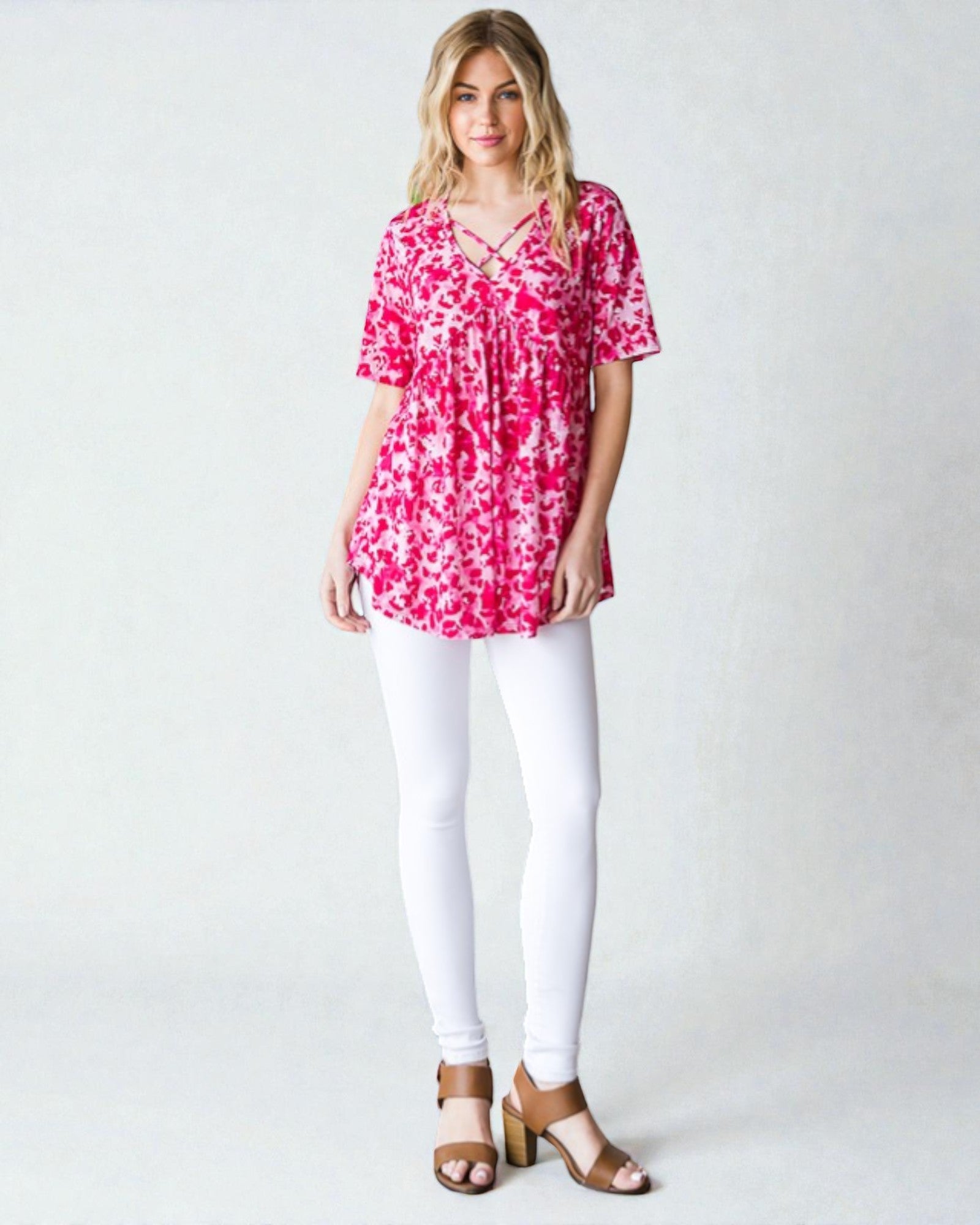 Woman wearing a pink floral top and white pants on a plain background