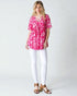 Woman wearing a pink floral top and white pants on a plain background