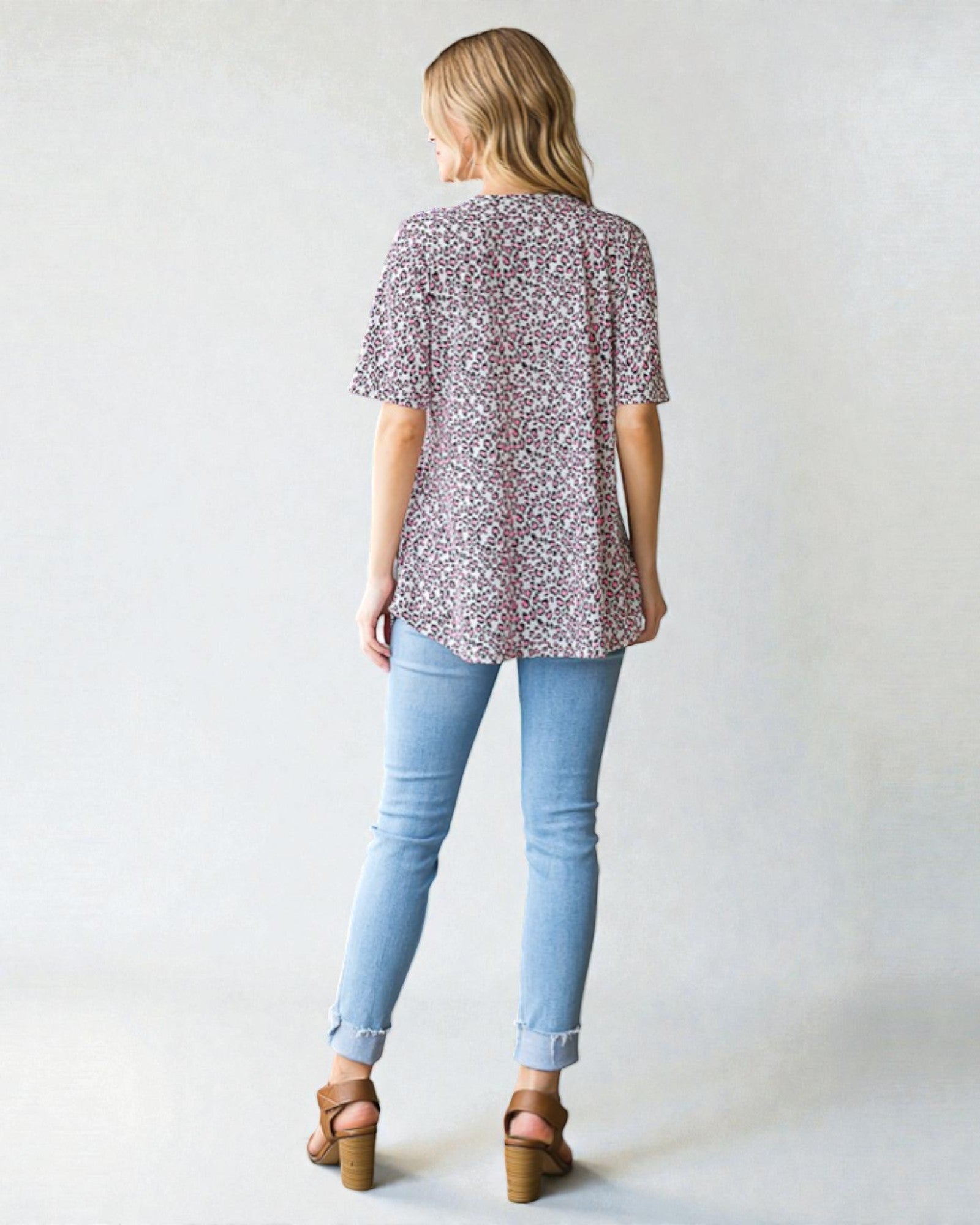 Woman wearing a patterned blouse and light blue jeans against a plain background