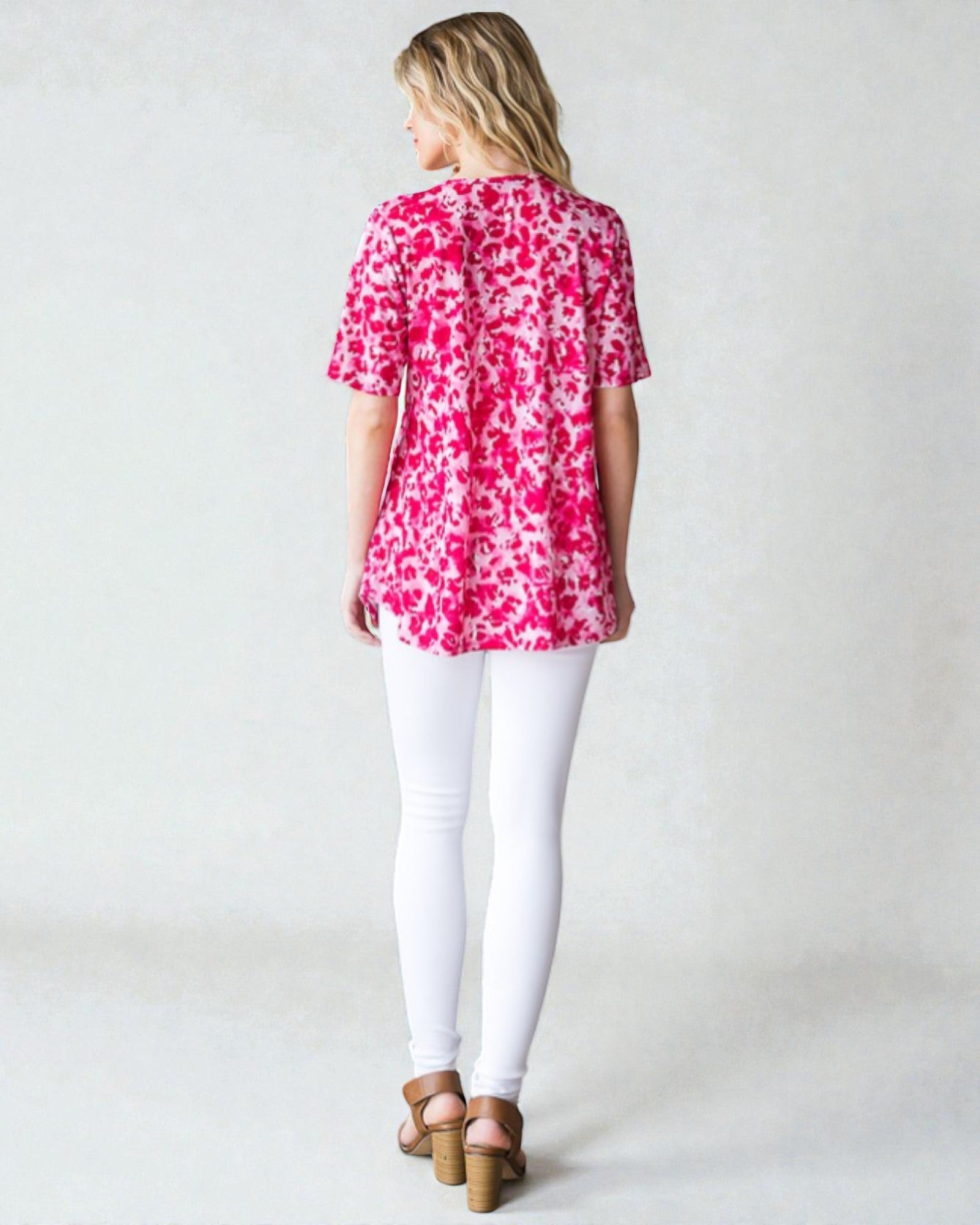 Woman wearing a pink floral blouse and white pants on a plain background