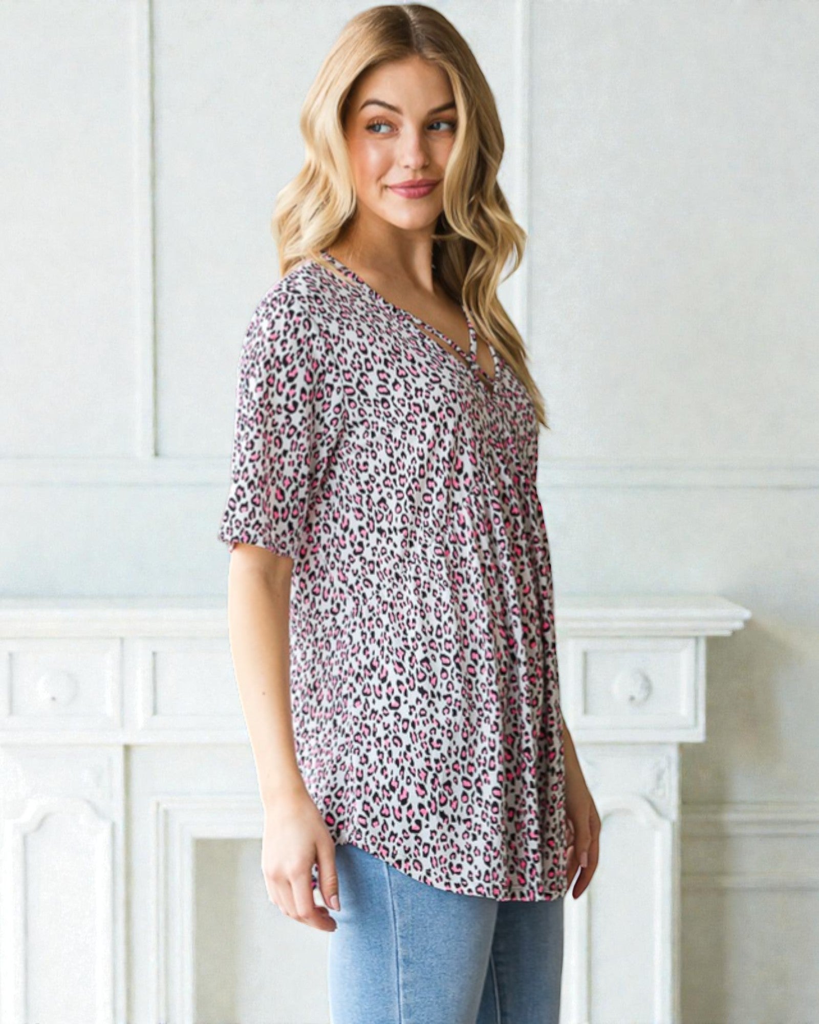 Woman wearing a patterned blouse and jeans standing in front of a white fireplace.