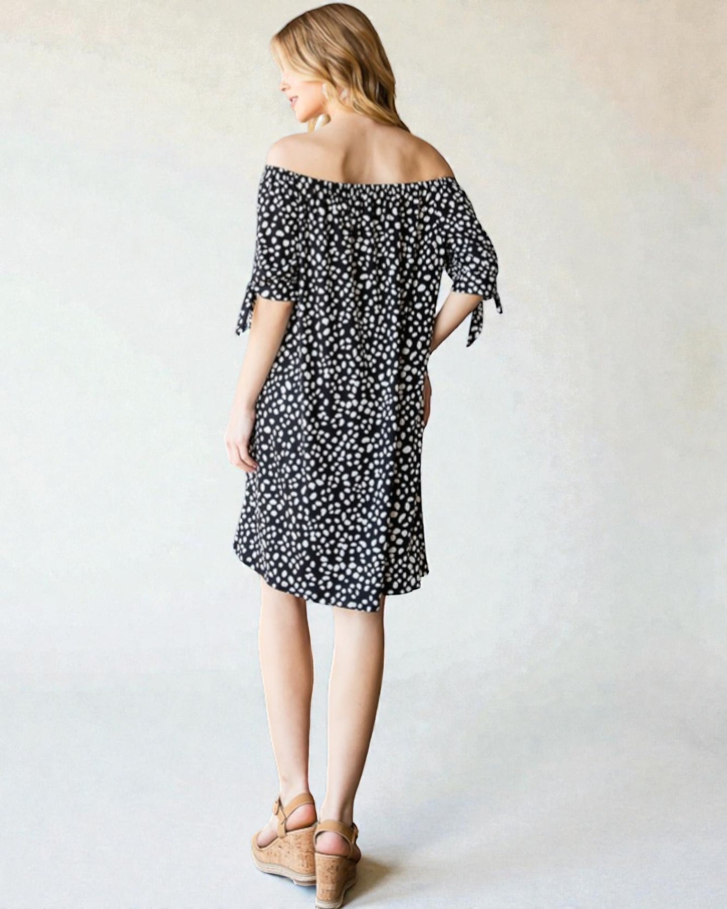 Woman wearing a black floral off-shoulder dress against a plain background