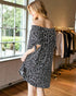 Woman wearing a black and white polka dot off-shoulder dress in a clothing store.