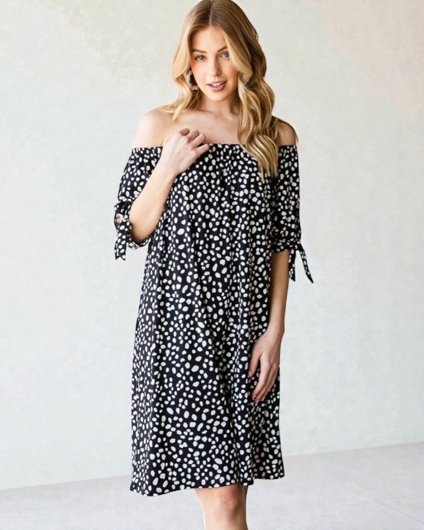 Woman wearing a black and white polka dot off-shoulder dress against a plain background