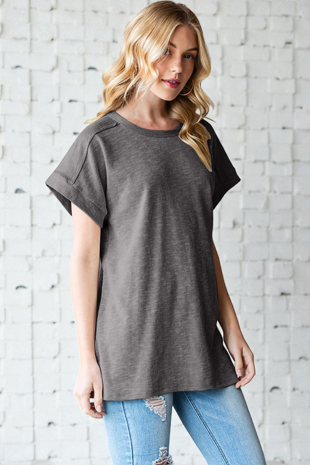Woman wearing a gray oversized t-shirt and light blue jeans against a white brick wall.