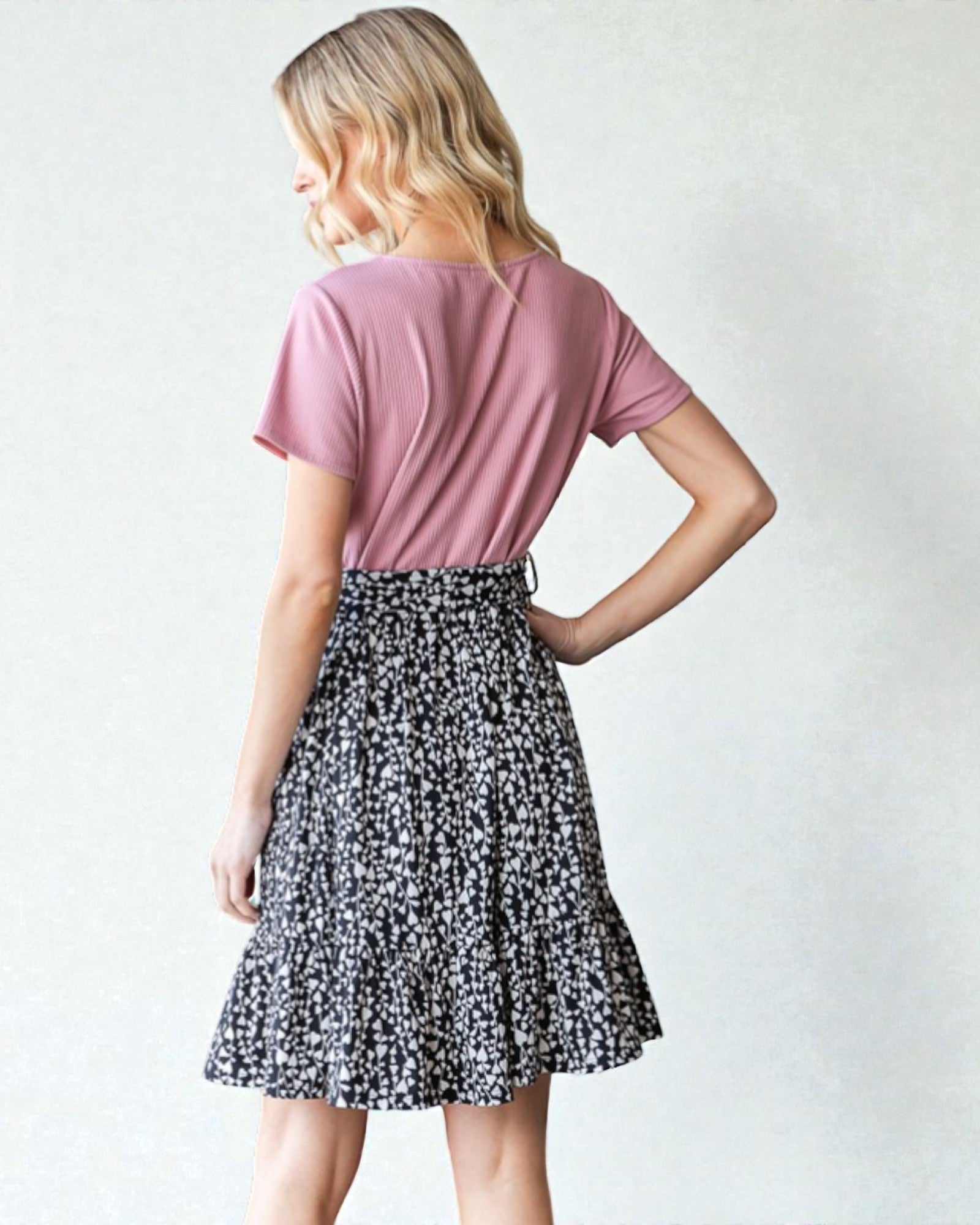 Woman wearing a pink top and black and white patterned skirt on a plain background