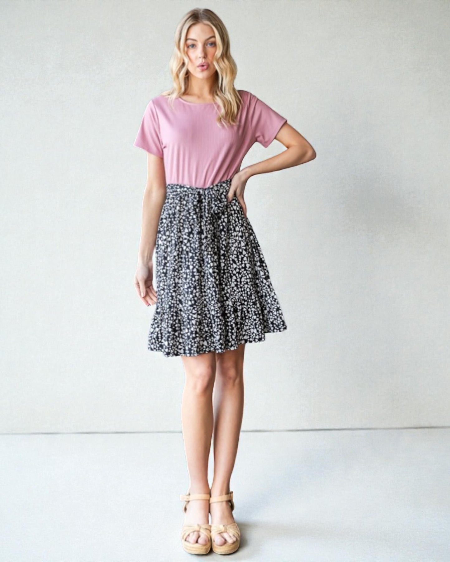 Woman wearing a pink top and patterned skirt against a plain background