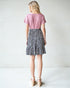 Person wearing a pink top and black and white patterned skirt on a white background