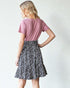 Woman wearing a pink top and black and white patterned skirt on a plain background