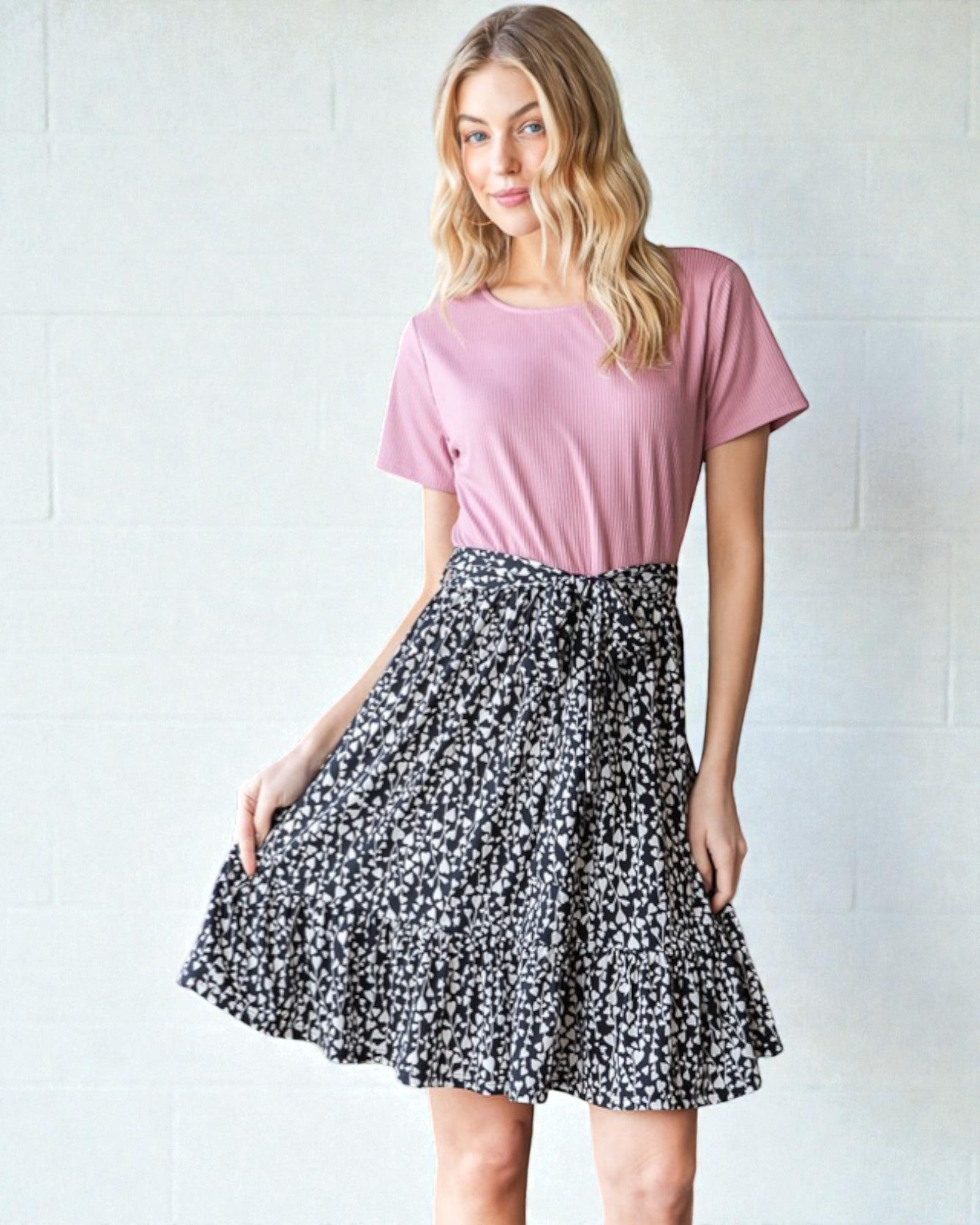 Woman wearing a pink top and black floral skirt against a white background