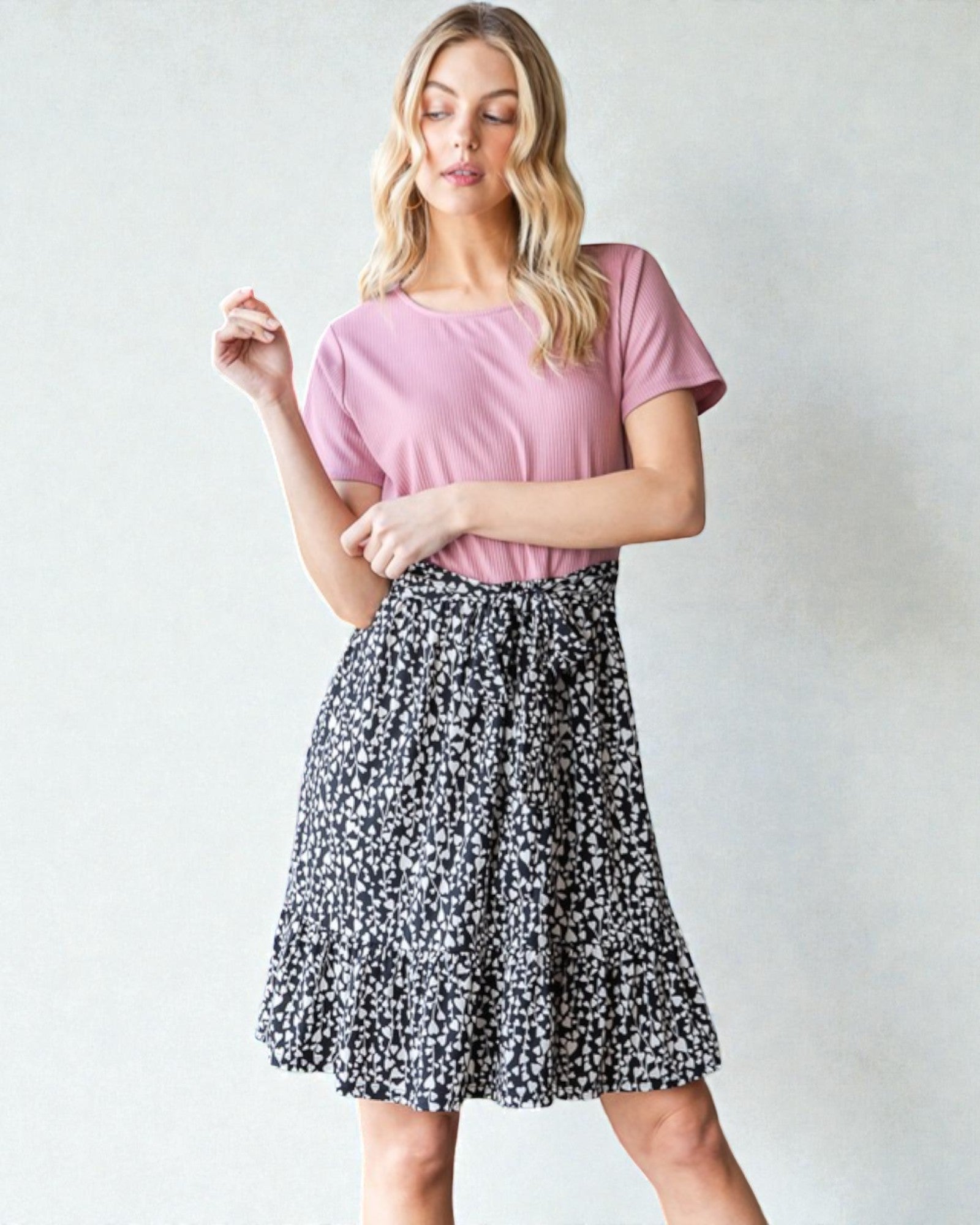 Woman wearing a pink top and black floral skirt on a white background