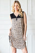Woman wearing a leopard print dress with a black top against a white wall.